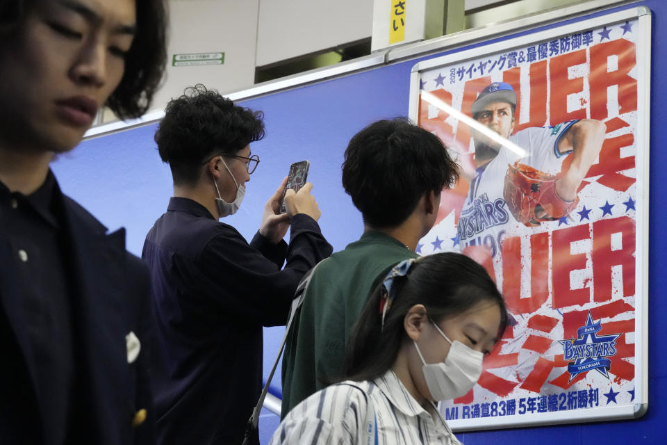 A passenger takes a photo of a poster of Trevor Bauer who's pitching for the Yokohama BayStars at a train station on Tuesday, May 2, 2023, in Yokohama near Tokyo. Bauer will pitch his first official game for the Yokohama DeNA BayStars on Wednesday and, to promote the start, a local department store is to unveil a seven-story poster of the former Cy Young winner on the building's facade. (AP Photo/Eugene Hoshiko)