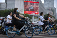 People cross an intersection near a large video screen showing Chinese President Xi Jinping speaking during an event to commemorate the 100th anniversary of China's Communist Party at Tiananmen Square in Beijing, Thursday, July 1, 2021. China's ruling Communist Party is marking the 100th anniversary of its founding with speeches and grand displays intended to showcase economic progress and social stability to justify its iron grip on political power. (AP Photo/Mark Schiefelbein)