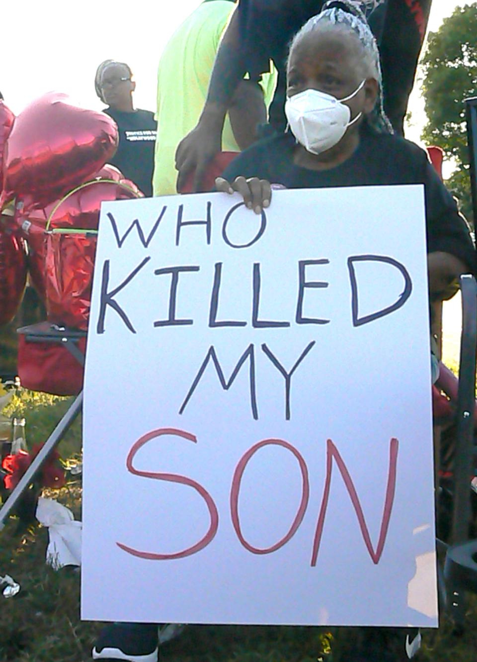 Vellogie Butler, 69, gathered at the spot where her son, Ronald Butler was fatally shot on July 19th. Sitting in a chair, she holds a sign "Who Killed My Son." Family and friends held a justice walk Tuesday along Mill Road where Butler was killed to encourage eyewitnesses to come forward.