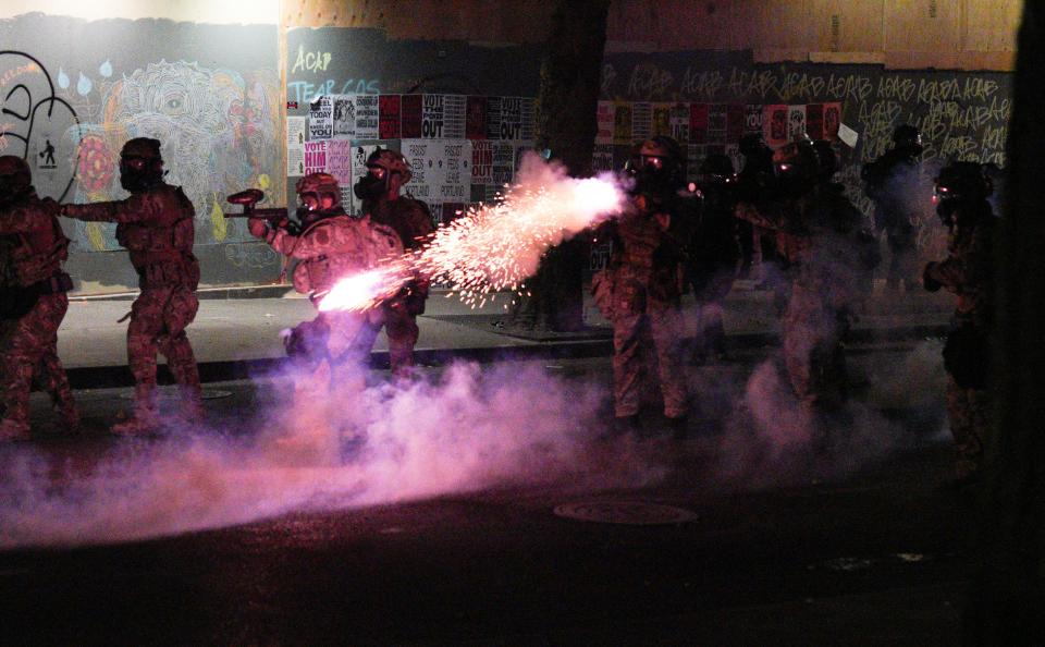 Federal agents form a defensive line and one fires a tear gas gun at advancing protesters outside the federal courthouse in Portland, Oregon, in the early hours of July 27, 2020.