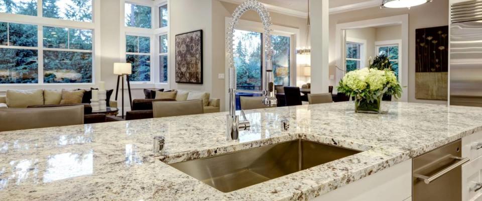 White kitchen design features large bar style kitchen island with granite countertop illuminated by modern pendant lights. Northwest, USA