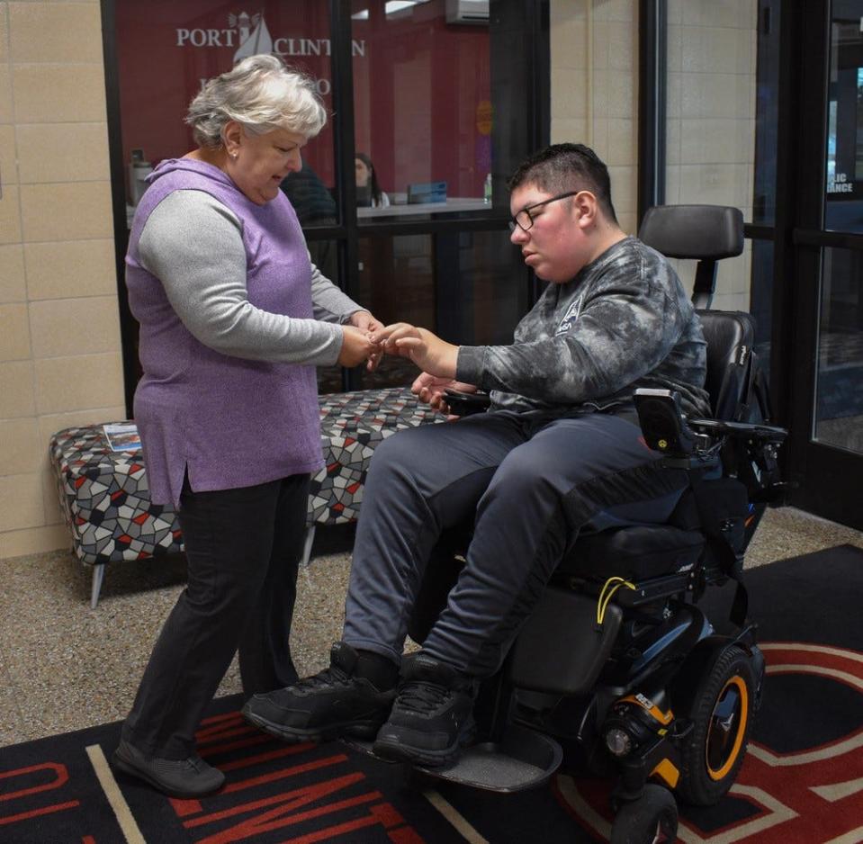 Port Clinton High School student Peyton Howard greets Walking Club member Pam Migot and gives her an ID badge at the school’s main entrance on Dec. 15.