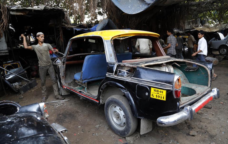 In this Wednesday, March 26, 2014 photo, a worker dismantles a taxi at a junk yard in Mumbai, India. The distinctive black-and-yellow licensed cabs number just 42,000 in Mumbai, inadequate for a city of 22 million. Taxi-hailing smartphone app Uber is making a big push into Asia with the company starting operations in 18 cities in Asia and the South Pacific including Seoul, Shanghai, Bangkok, Hong Kong and five Indian cities in the last year. (AP Photo/Rajanish Kakade)