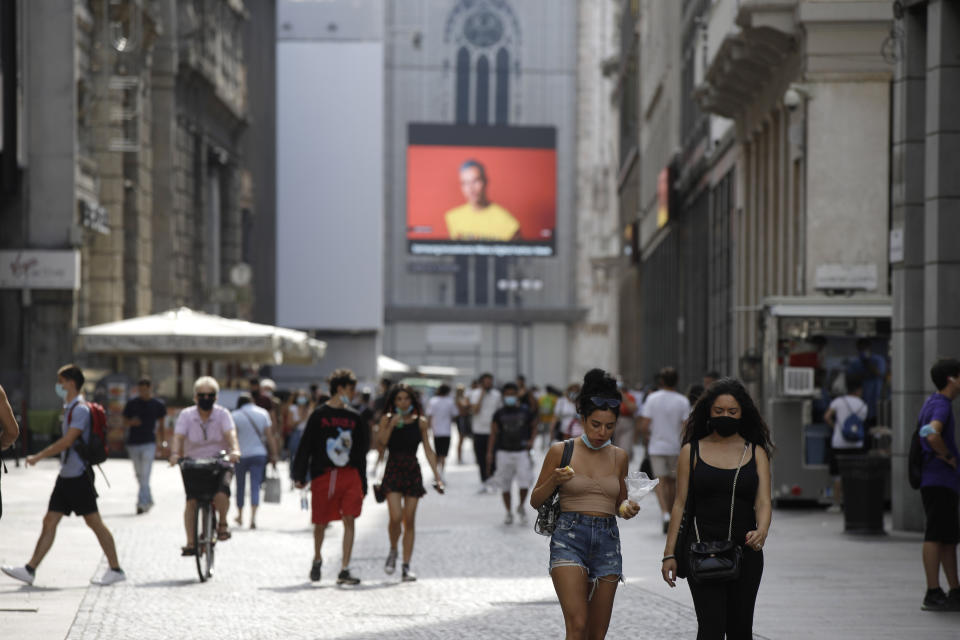 Pedestrians pass by a screen on the Duomo cathedral, showing a Moschino model during the Milan Digital Fashion Week, in Milan, Italy, Tuesday, July 14, 2020. Forty fashion houses are presenting previews of menswear looks for next spring and summer and pre-collections for women in digital formats, due to concerns generated by the COVID-19. (AP Photo/Luca Bruno)