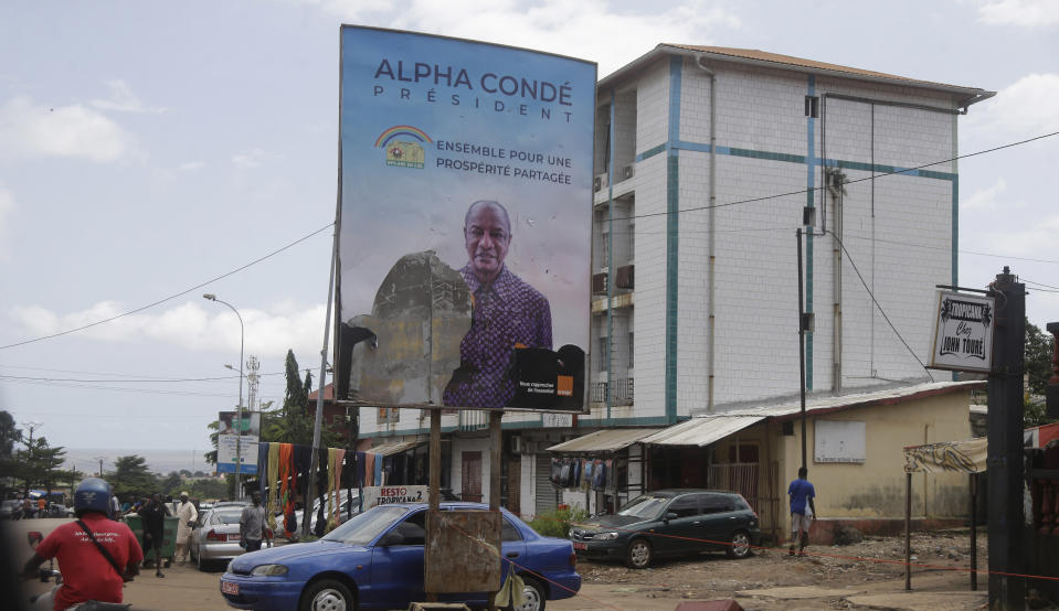 People walk past a defaced billboard with former Guinea's President Alpha Conde, on a street in Conakry, Guinea, Thursday, Sept. 9, 2021. Guinea's new military leaders sought to tighten their grip on power after overthrowing President Alpha Conde, warning local officials that refusing to appear at a meeting convened Monday would be considered an act of rebellion against the junta. (AP Photo/Sunday Alamba)