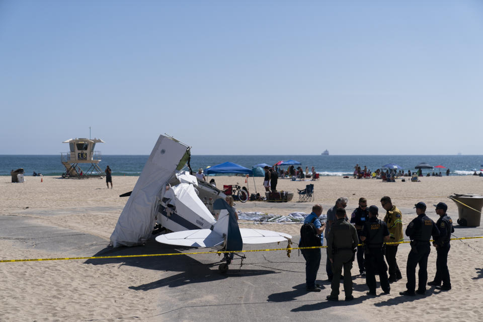 Investigators stand next to a small plane that was pulled from the water after it crashed into the ocean in Huntington Beach, Calif., Friday, July 22, 2022. The plane towing a banner crashed in the ocean Friday during a lifeguard competition that turned into a real-life rescue along the popular beach. (AP Photo/Jae C. Hong)