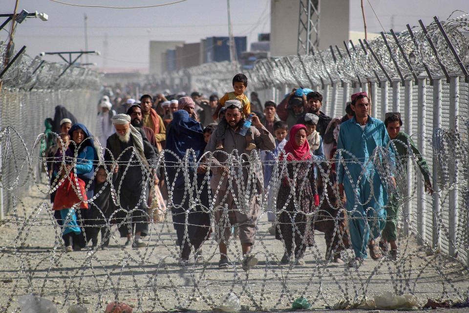 Afghans walk along fences as they arrive in Pakistan through the Pakistan-Afghanistan border crossing point in Chaman on Aug. 24, 2021, following Taliban's military takeover of Afghanistan.