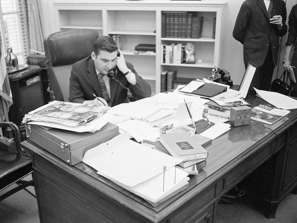 White House Press Secretary Pierre Salinger speaks on the phone surrounded by papers on a desk during his time with the Kennedy administration in 1961.