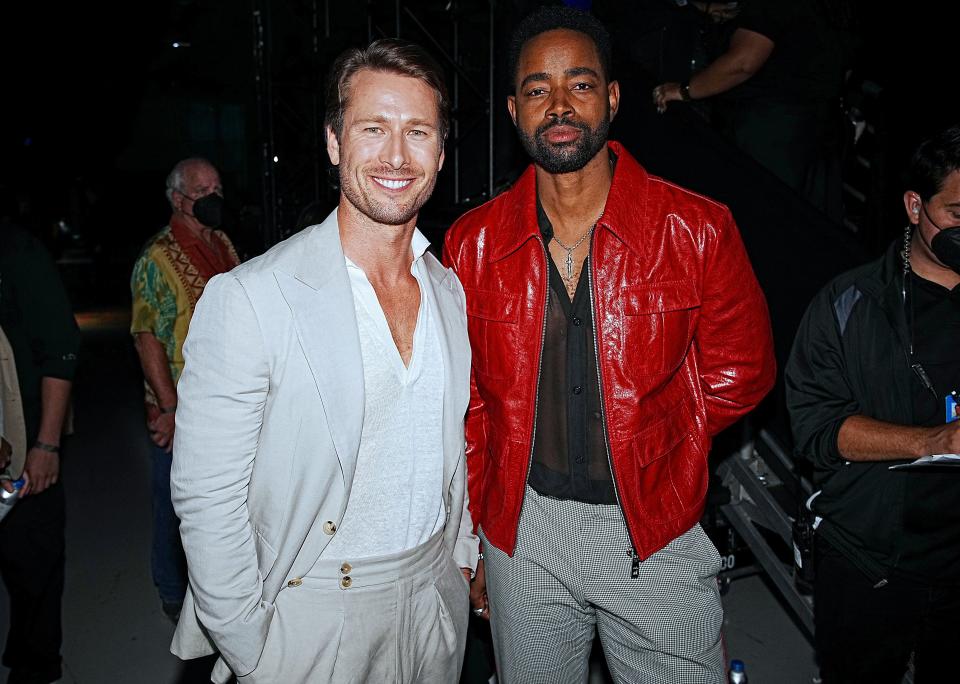Glen Powell in a cream jacket standing next to Jay Ellis in a red jacket