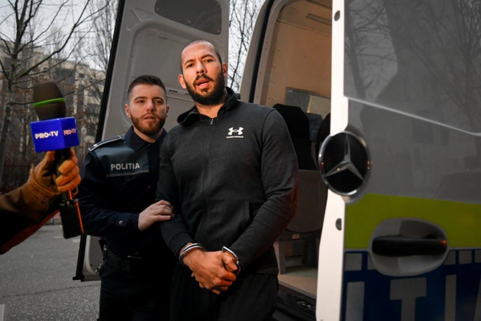 Agentes de policía escoltan a Andrew Tate fuera de la DIICOT (Dirección de Investigación de la Delincuencia Organizada y el Terrorismo), donde los fiscales examinan los equipos electrónicos confiscados durante la investigación de su caso, en Bucarest, Rumanía (AP)