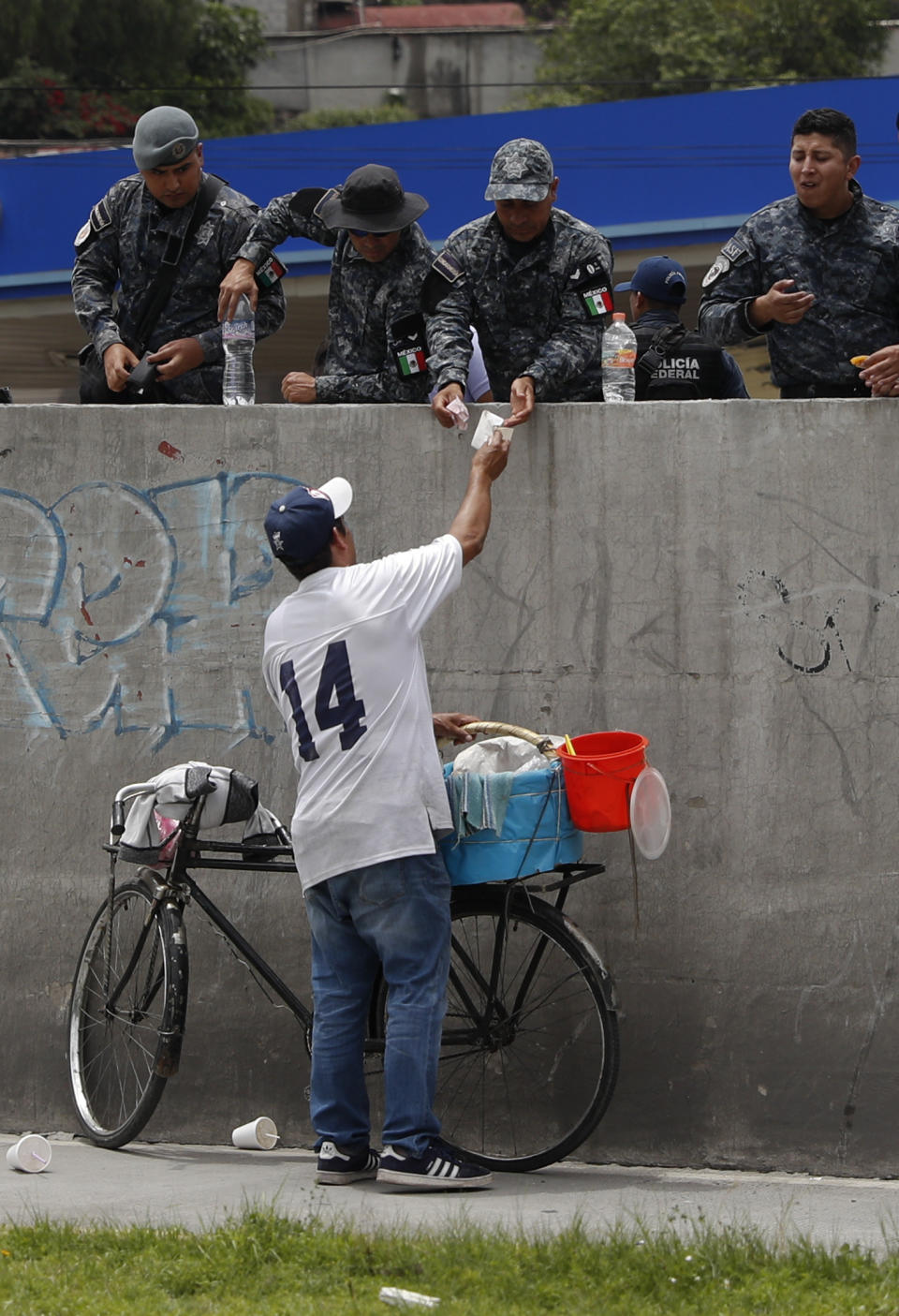 A bike vendor sells tacos to federal police maintaining a roadblock on both directions of the highway linking Mexico City with Pachuca, in Ecatepec, Wednesday, July 3, 2019. Hundreds of Mexican federal police were in open revolt Wednesday against plans to absorb them into the newly formed National Guard.(AP Photo/Rebecca Blackwell)