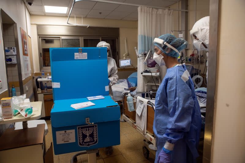 Hospital employees stand next to a mobile voting booth and box as they make their way to assist patients in a ward for the treatment of the coronavirus disease (COVID-19), to vote in Israel's general election, at Sheba Medical Center in Ramat Gan