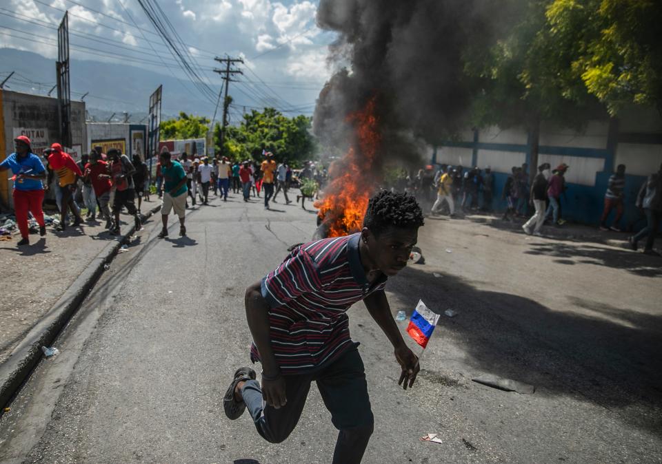 Protesters walk past burning tires during a protest to reject an international military force requested by the government and demand the resignation of Prime Minister Ariel Henry in Port-au-Prince, Haiti, on Monday, Oct. 17, 2022. The United Nations Security Council is evaluating the request by the Haitian government for the immediate deployment of foreign troops to help free Haiti from the grip of gangs that has caused a scarcity of fuel, water, and other basic supplies.
