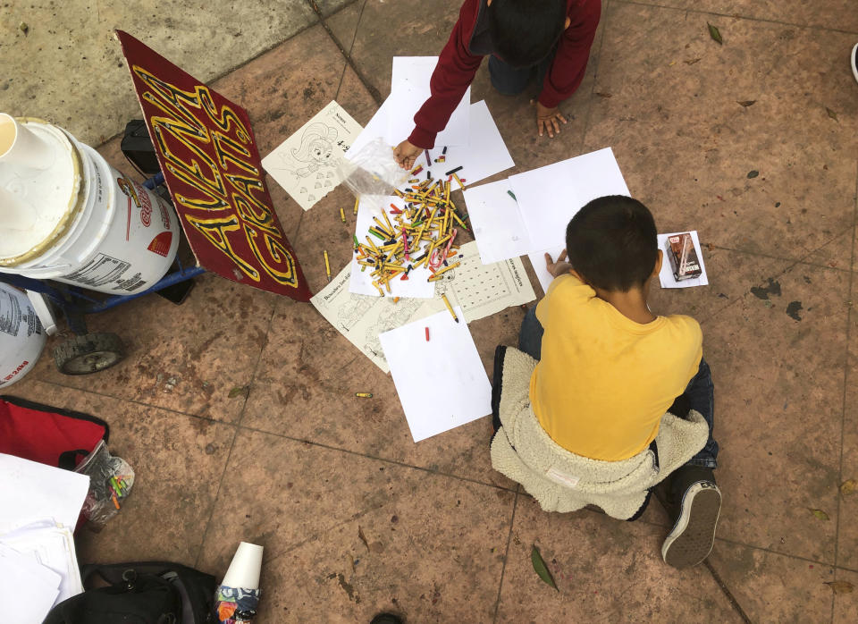 A Mexican boy draws with crayons while his family waits in Tijuana, Mexico, for their names to be called from a waiting list to claim asylum at a border crossing in San Diego Thursday, Sept. 26, 2019. An advocacy group served free oatmeal at left. The Trump administration played "bait and switch" by instructing migrants to wait in Mexico for an opportunity to apply for asylum before imposing sharp restrictions on eligibility, attorneys said in a court filing Thursday. (AP Photo/Elliot Spagat)