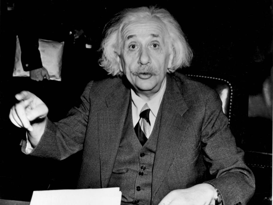 albert einstein wears a suit and sits in a chair