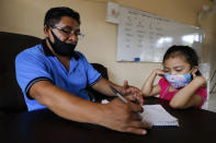 Wearing masks to curb the spread of the new coronavirus, a teacher checks the work of his 10-year-old student Jade Chan Puc during the first day of class at the Valentín Gomez Farias Indigenous Primary School in Montebello, Hecelchakan, Campeche state, Monday, April 19, 2021. Campeche is the first state to transition back to the classroom after a year of remote learning due to the pandemic. (AP Photo/Martin Zetina)