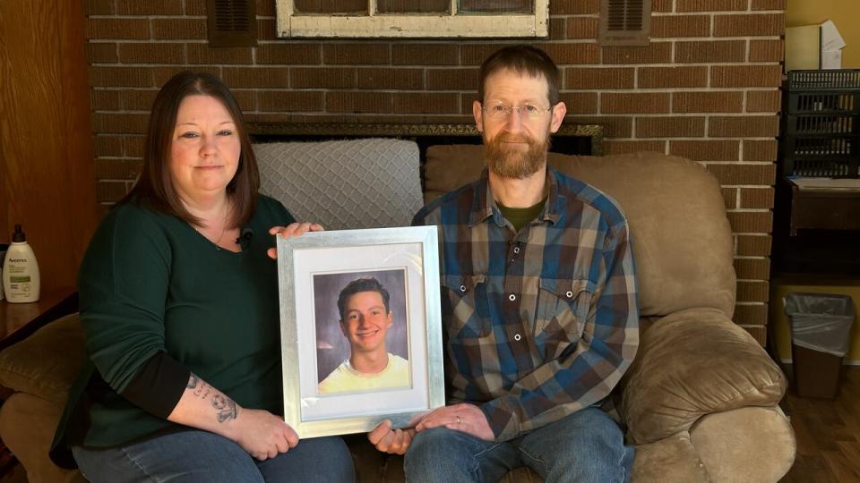 Amy and Greg Hoyt with a school photo of their son, Carson, who died by suicide in June 2021 at the age of 15. 