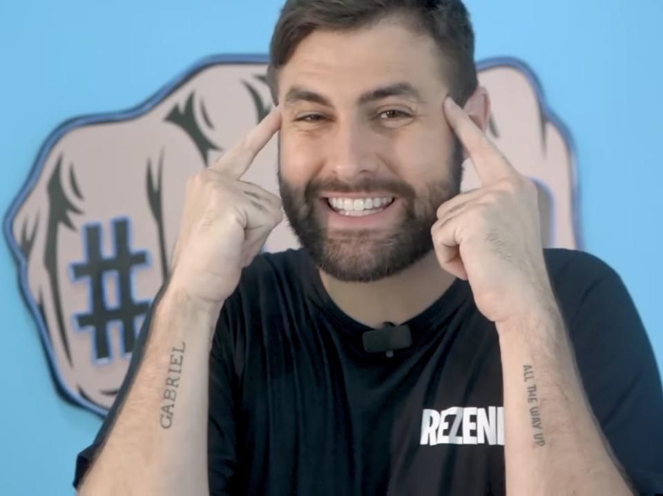 Screenshot from one of Rezende's videos, in front of a blue background with his pointer fingers on his temples.