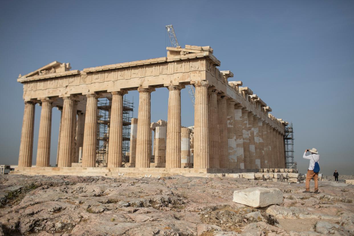 A man takes a picture next the ancient Parthenon temple at the Acropolis hill of Athens on Monday, May 18, 2020. Greece reopened the Acropolis in Athens and other ancient sites Monday, along with high schools, shopping malls, and mainland travel in the latest round of easing pandemic restrictions imposed in late March.