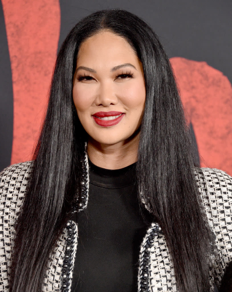 Kimora Lee Simmons smiles, wearing a patterned blazer over a black top, with long straight hair styled neatly