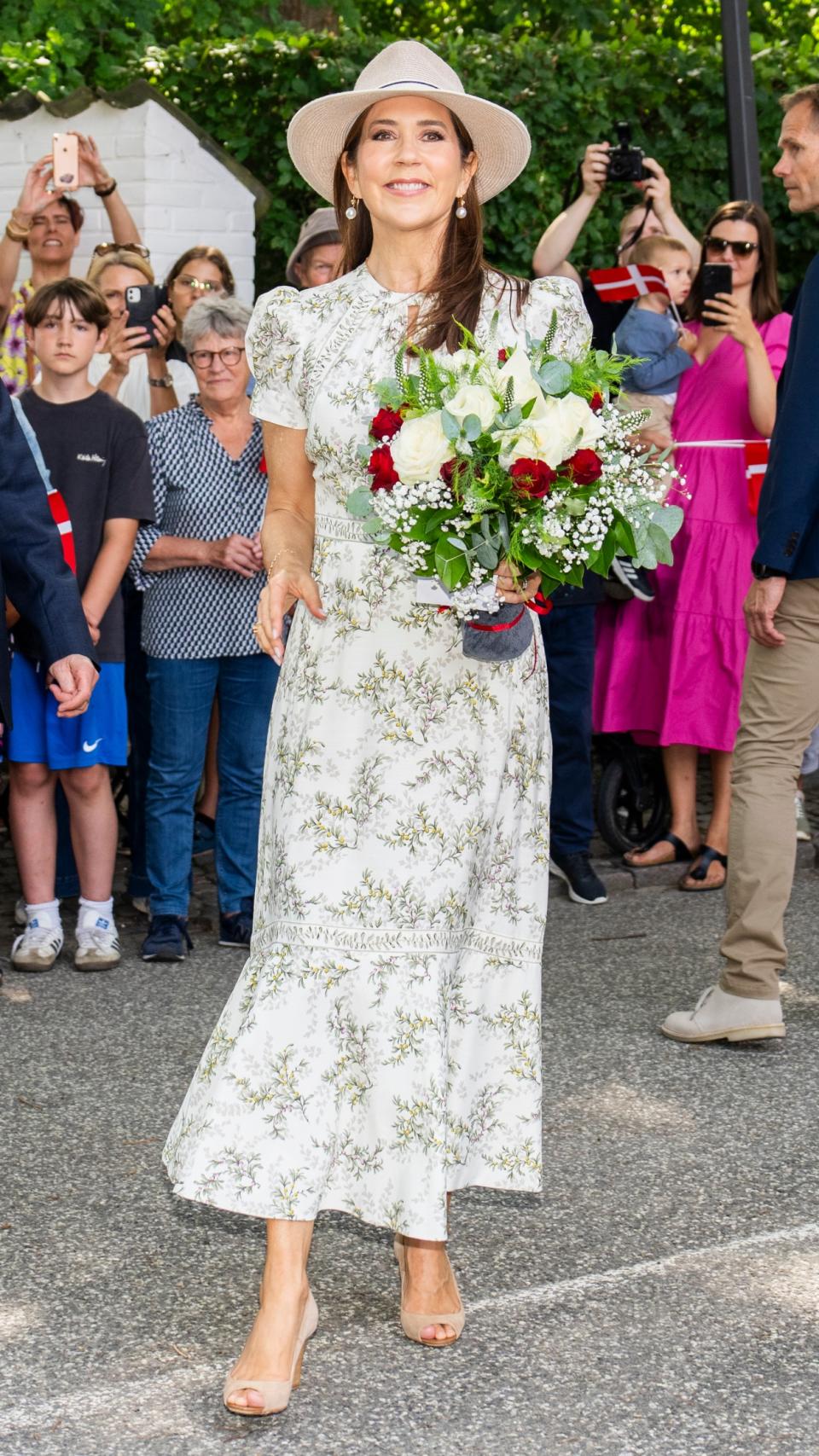 Queen Mary of Denmark, wearing a sunhat, green floral dress and wedges, is welcomed by the public as she arrives in Gråsten,