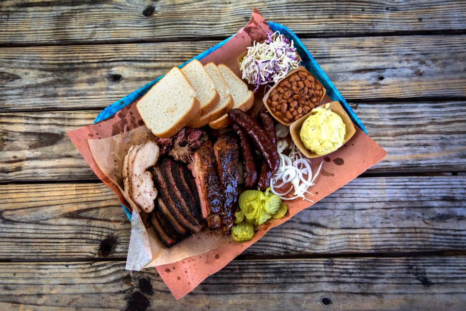 A tray of smoked turkey, brisket, ribs, sausage alongside coleslaw, baked bean, Wonder bread and potato salad can be seen at Franklin Barbecue in 2019.