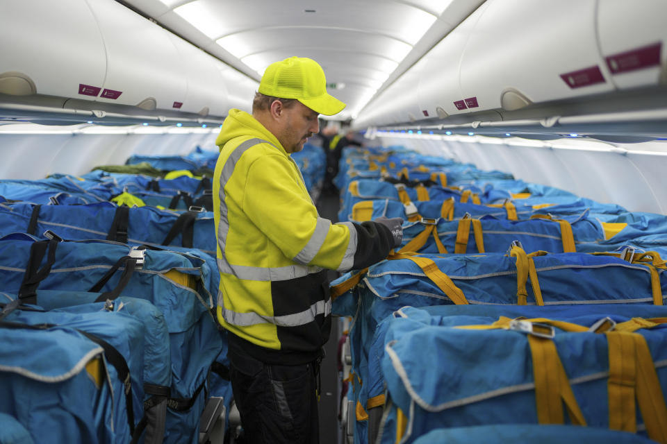 A WISAG employee secures plastic boxes full of mail covered with fabric sleeves to the passenger seats of an Airbus A320-214 at Berlin Brandenburg Airport, in Schönefeld, Germany, Thursday, March 28, 2024. Germany's main national postal carrier on Thursday put an end to domestic flights to transport letters, stopping the practice after nearly 63 years in a move that will allow it to improve its climate footprint and reflects the declining significance of letter mail. (Soeren Stache/dpa via AP)