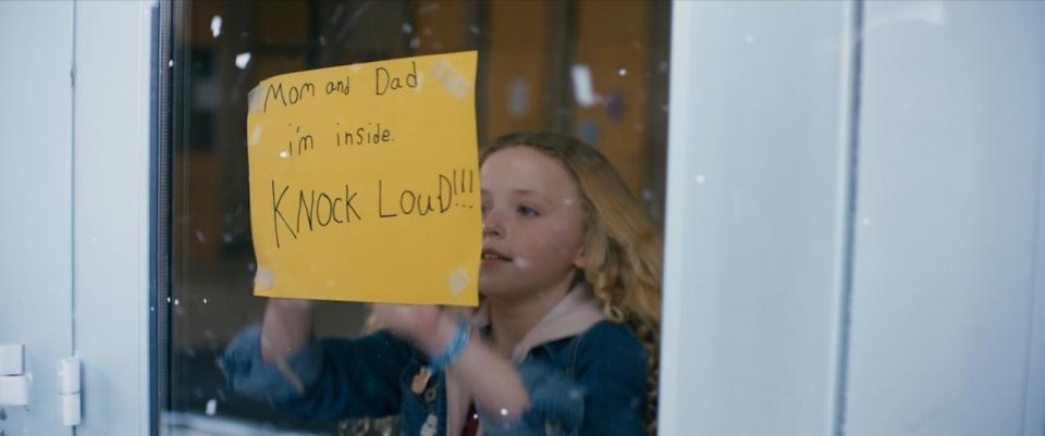 A girl sticks a notice on the glass portion of a door of her school.