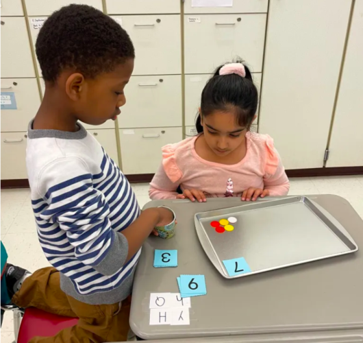 Two kindergarten students at Hilltop Elementary in Aston, Pennsylvania., play a guess-the-number game with different colored counters. (Holly Korbey/The Hechinger Report)