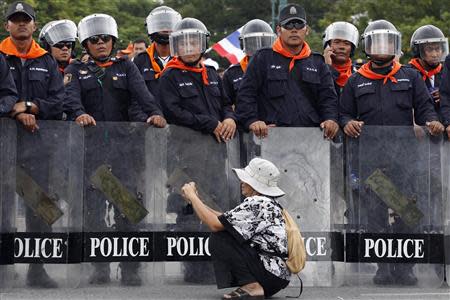 A woman takes pictures in front of a line of policemen blocking protesters against an amnesty bill, on the main road near the government and parliament buildings in central Bangkok November 7, 2013. REUTERS/Kerek Wongsa