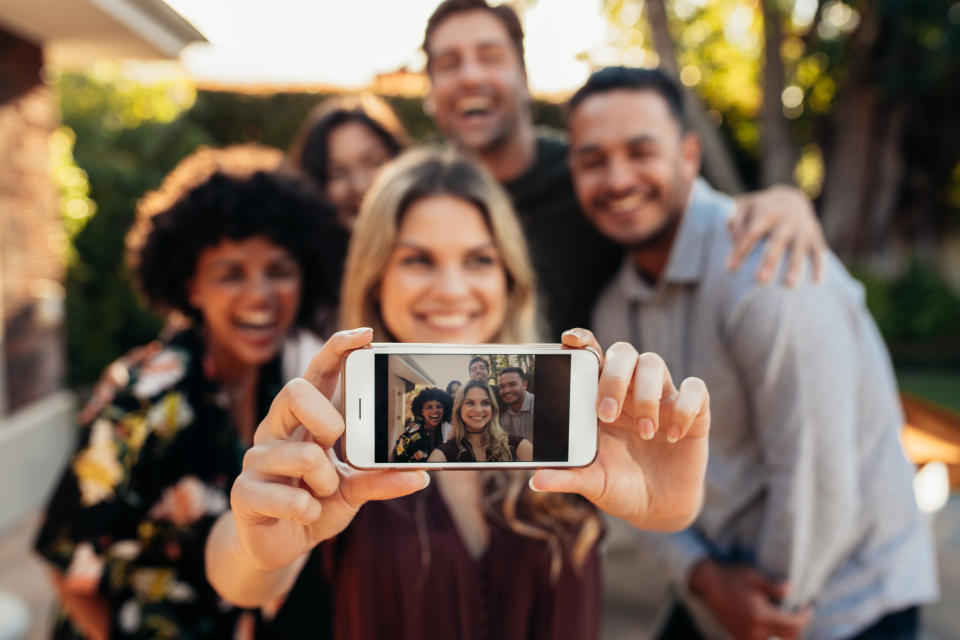 Happy young friends having fun at party taking selfie. Focus on mobile phone in hands of female.