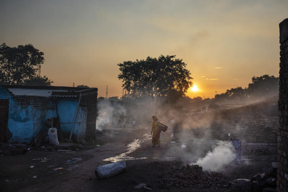 A woman walks past piles of coal burning after scavenging from an open-cast mine near Dhanbad, an eastern Indian city in Jharkhand state, Thursday, Sept. 23, 2021. On Saturday, India asked for a crucial last minute-change to the final agreement at crucial climate talks in Glasgow, calling for the "phase-down" not the "phase-out" of coal power. (AP Photo/Altaf Qadri)