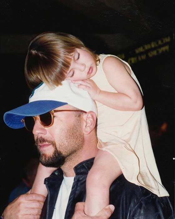 A young Scout Willis sat on the shoulders of her father Bruce, who is wearing sunglasses and a sun hat