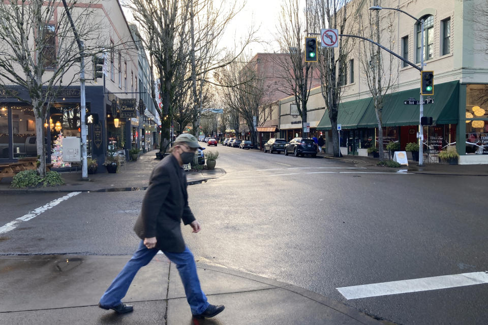 A pedestrian starts to cross a street in McMinnville, Ore., on Thursday, Dec. 9, 2021. Like many other towns in the U.S., McMinnville was hit by the opioid epidemic, leaving overdoses, addiction, homelessness and wrecked families in its wake. States, counties and cities are on the precipice of receiving billions of dollars in the second-biggest legal settlement in U.S. history. (AP Photo/Andrew Selsky)