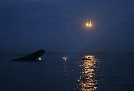 South Korean ferry "Sewol" (L) is seen sinking at the sea off Jindo, as lighting flares are released for a night search, April 16, 2014. REUTERS/Kim Hong-Ji