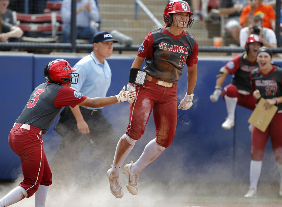 FILE - Oklahoma's Nicole Mendes (11) and Kelsey Arnold (3) celebrate scoring in the fifth inning during the Women's College World Series softball game between the against Oregon at ASA Hall of Fame Stadium in Oklahoma City, in this Sunday, June 4, 2017. Division I softball is providing a training ground this season for players preparing for the 2021 Olympics. Oklahoma’s Nicole Mendes and North Carolina State’s Tatyana Forbes will play for Mexico, their schools said. (Sarah Phipps/The Oklahoman via AP, File)