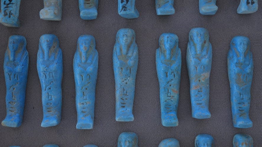 Little figurines of mummies, made out of blue material, are shown here lined up side by side
