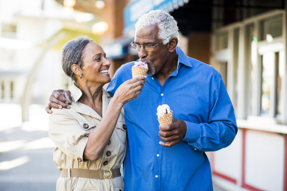 An older couple enjoying ice cream cones on a sunny day, smiling and appearing happy in a casual outdoor setting