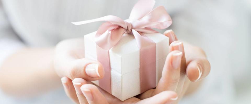 Close up shot of female hands holding a small gift wrapped with pink ribbon. Small gift in the hands of a woman indoor. Shallow depth of field with focus on the little box.