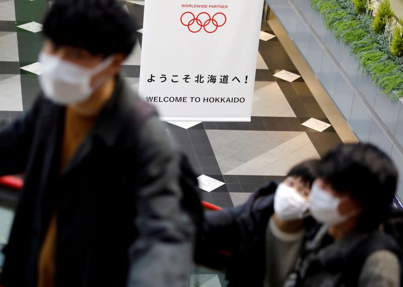 FILE PHOTO: Passengers wearing protective face masks, following an outbreak of the coronavirus, are seen near a campaign banner for Tokyo 2020 Olympic Games at New Chitose Airport in Chitose, Hokkaido