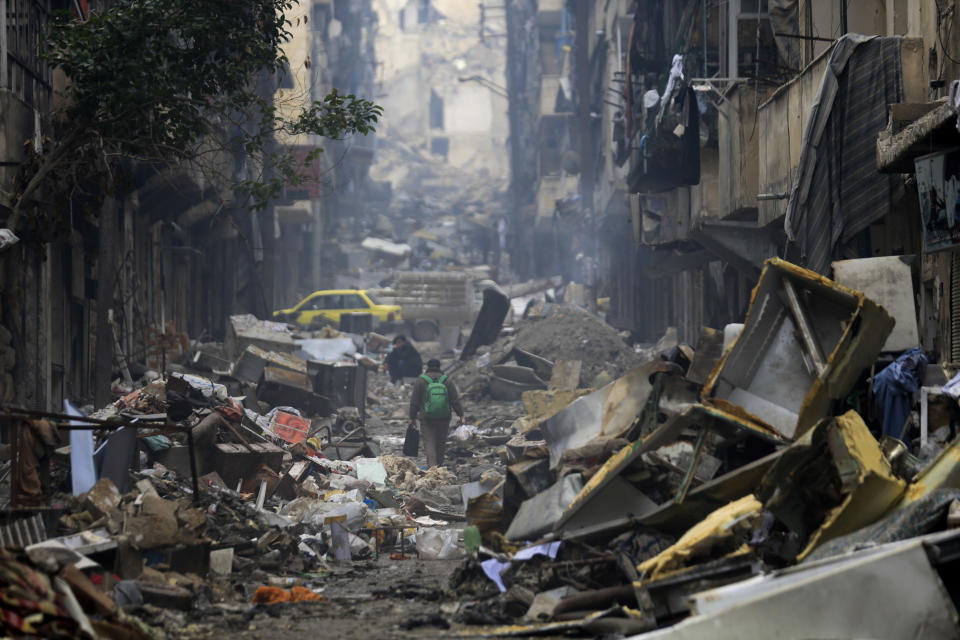 FILE - In this Jan. 20, 2017 file photo, residents walk through the destruction of the once rebel-held Salaheddine neighborhood in the eastern Aleppo, Syria. Syrians are marking 10 years since peaceful protests against President Bashar Assad's government began in March 2011, touching off a popular uprising and a war that turned into the worst humanitarian crisis of the 21st century. (AP Photo/Hassan Ammar, File)