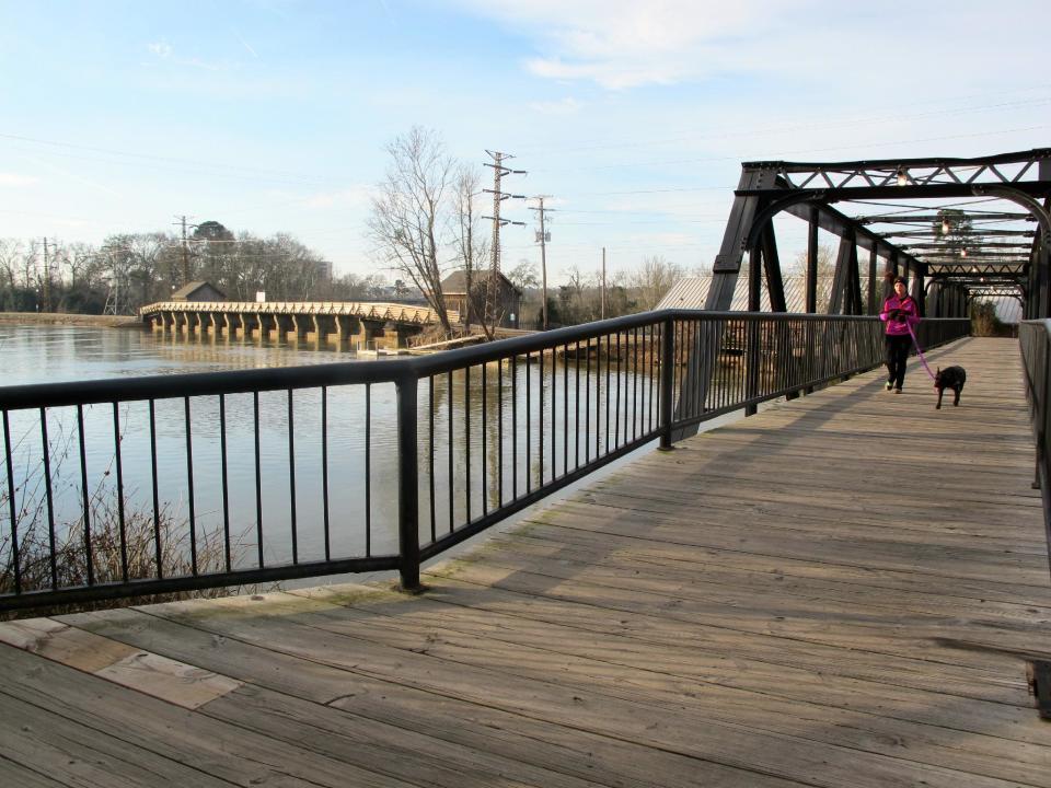 A jogger and her dog run across a bridge at the Columbia Riverfront Park in Columbia, S.C., on Jan. 25, 2014. For years, South Carolina's capital was known mainly to visitors as the seat of state government and the home of the University of South Carolina. But in recent years the area's varied attractions have been marketed as part of tourism campaign that the area is "Famously Hot." An estimated 1 million visitors a year now visit the area. (AP Photo/Bruce Smith)