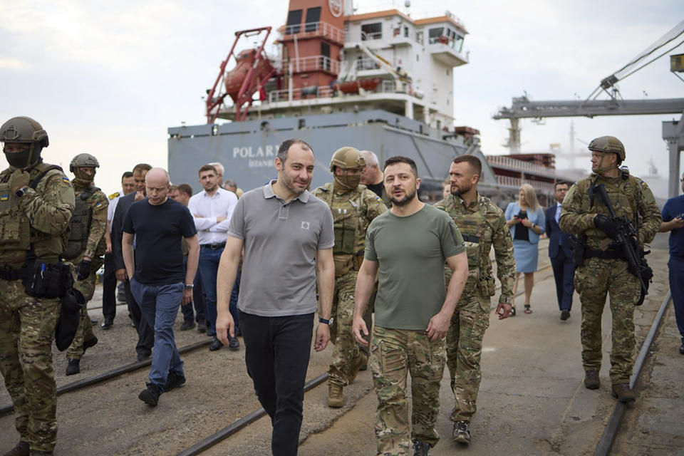 In this photo provided by the Ukrainian Presidential Press Office, Ukrainian President Volodymyr Zelenskyy, center, surrounded by ambassadors of different countries and UN officials, visits a port in Chornomork during loading of grain on a Turkish ship, background, close to Odesa, Ukraine, Friday, July 29, 2022. (Ukrainian Presidential Press Office via AP)