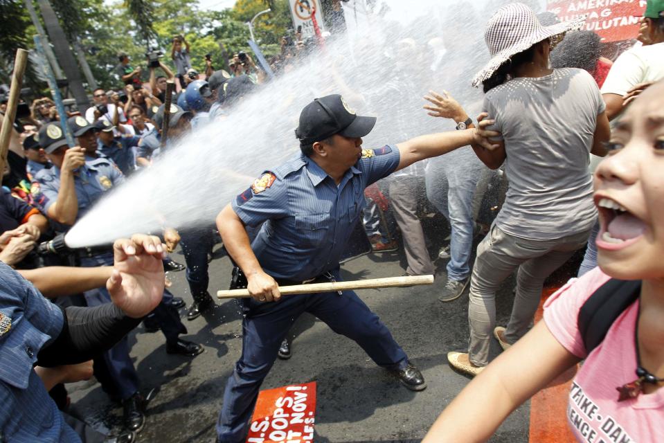 An anti-riot policeman reaches to grab a protester as they are hit with a water cannon during a protest against the upcoming visit of U.S. President Barack Obama next week, in front of the U.S. embassy in Manila