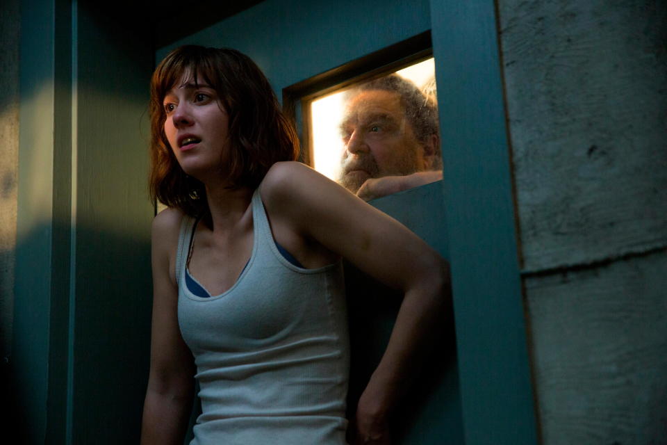 Mary Elizabeth Winstead as Michelle, pressed against a door, while John Goodman as Howard Stambler looks through its window in 10 Cloverfield Lane