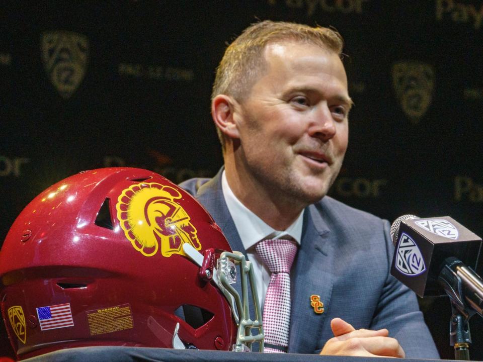 Lincoln Riley smiles while speaking at a press conference.