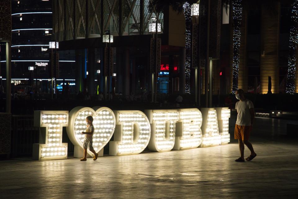 A man and a boy walk by a "I Love Dubai" sign at the Dubai Mall while wearing surgical masks over the coronavirus pandemic in Dubai, United Arab Emirates, Monday, May 11, 2020. Malls have opened back up across Dubai and the rest of the United Arab Emirates despite facing an ever-growing number of infections, part of efforts to stimulate the country's already-strained economy. (AP Photo/Jon Gambrell)