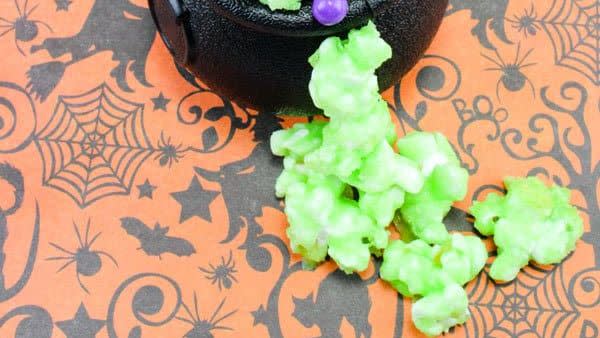 black mini cauldrons filled with a green popcorn mixed with candy eyes and colorful candies on orange halloween tablecloth