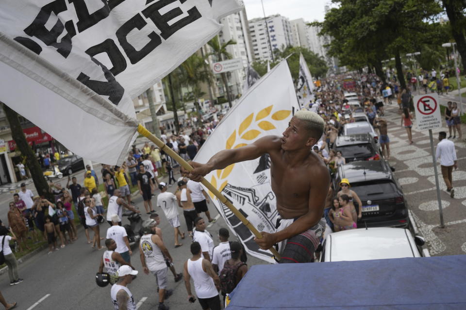 A fan waves a Santos FC soccer club flag along the route of the funeral procession for late Brazilian soccer great Pele, from Vila Belmiro stadium to the cemetery, in Santos, Brazil, Tuesday, Jan. 3, 2023. (AP Photo/Matias Delacroix)