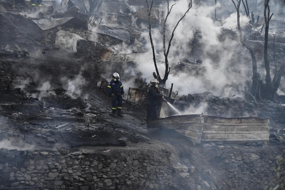 Firefighters spray water inside a refugee and migrant camp after a fire broke out, on the Greek island of Samos, Greece, Monday, Nov. 2, 2020. Dozens of accommodations were destroyed by the fire which broke out in the early hours on Monday, three days after an earthquake hit the island. (AP Photo/Michael Svarnias)